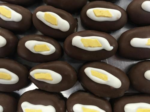 A close-up of chocolate-covered treats with a white icing swirl and a small yellow piece on top, arranged neatly.