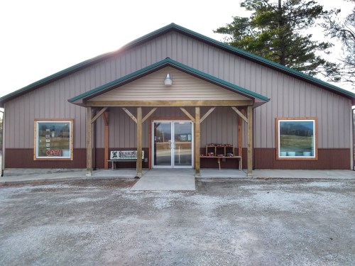 A large, brown building with a green roof and open sign, featuring a covered entrance and gravel pathway.