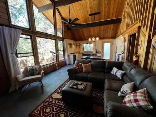 Cozy living room with wooden beams, large windows, a sectional sofa, and a view of nature outside.