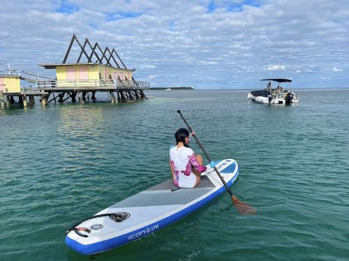 A person paddles on a stand-up paddleboard in calm waters near a colorful dock and a boat in the background.