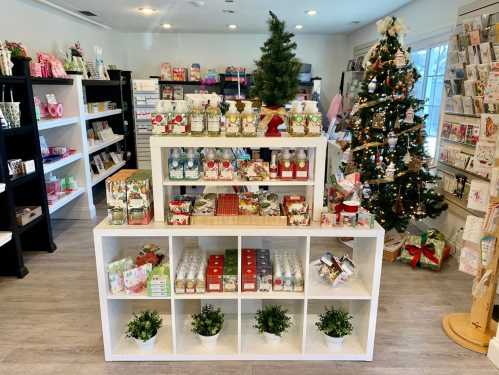 A festive shop display featuring holiday decorations, gift items, and a Christmas tree in a bright, inviting space.