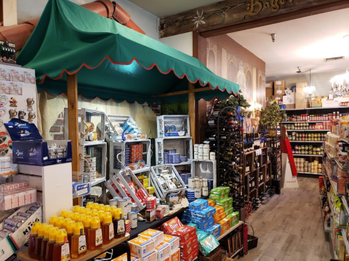 A cozy grocery store aisle filled with shelves of canned goods, honey, and wine, under a green canopy.