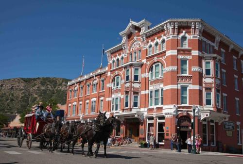 A horse-drawn carriage passes by a historic red brick hotel on a sunny day, with mountains in the background.