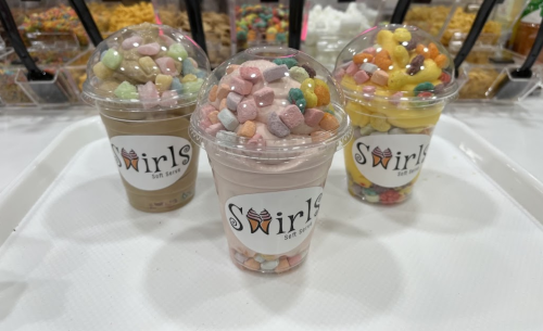 Three colorful ice cream cups topped with various sprinkles and marshmallows, displayed on a white tray.