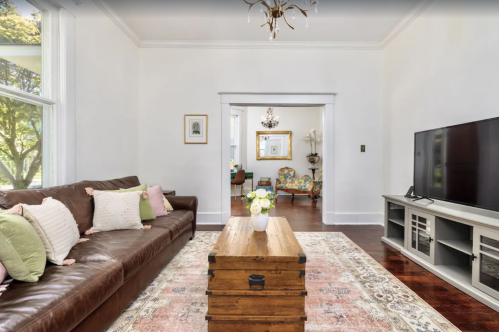Cozy living room with a brown leather sofa, wooden coffee table, and a TV, featuring light walls and decorative accents.