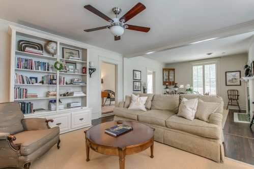 Cozy living room with a beige sofa, wooden coffee table, bookshelves, and a ceiling fan, featuring warm, inviting decor.