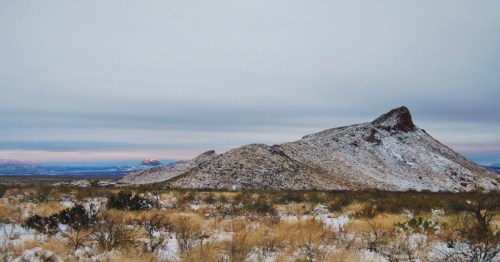 A snowy mountain landscape with rolling hills and a cloudy sky, showcasing a serene, wintry scene.