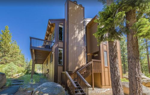 A modern wooden cabin surrounded by trees, featuring multiple levels and a deck.