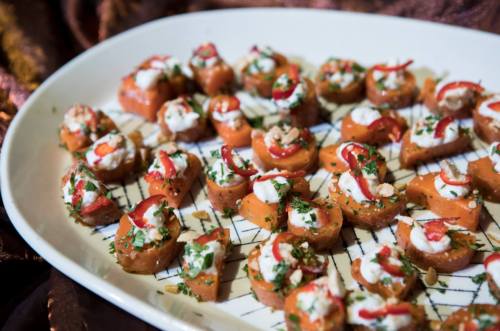 A platter of bite-sized appetizers topped with cream, herbs, and red chili on a decorative background.