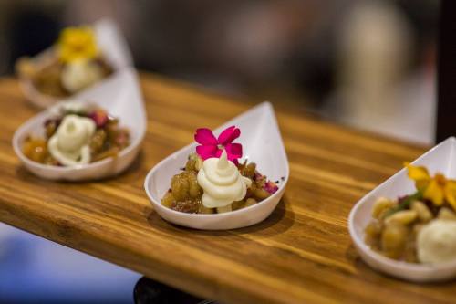 Elegant dessert cups on a wooden platter, topped with cream and colorful edible flowers.