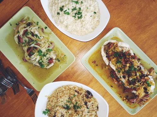 A table with four dishes: two fish plates with toppings, and two bowls of grain dishes, all garnished with herbs.