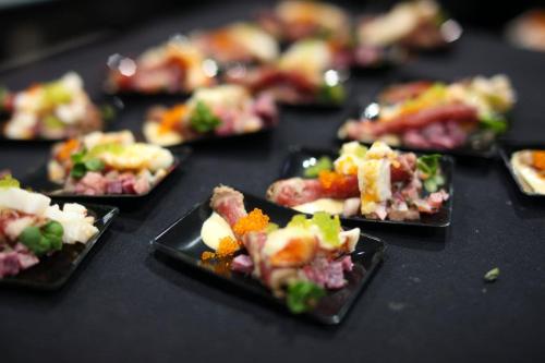 A close-up of gourmet appetizers on small black plates, featuring various meats, garnishes, and colorful toppings.