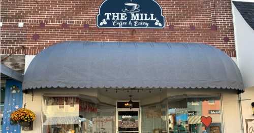 Exterior of "The Mill Coffee & Eatery," featuring a gray awning and a sign above the entrance. Flower pots adorn the entrance.