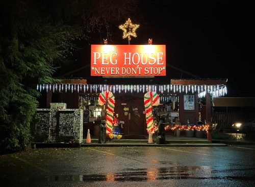 A brightly lit shop called "Peg House" with festive decorations and a star on top, illuminated at night.