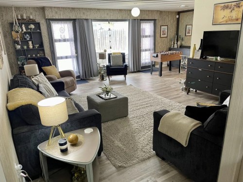 Cozy living room with two sofas, a coffee table, and a TV, featuring warm decor and natural light from large windows.