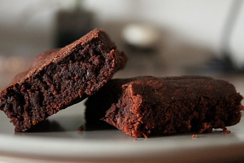 Two rich, fudgy brownies on a plate, one cut in half to reveal a moist interior.