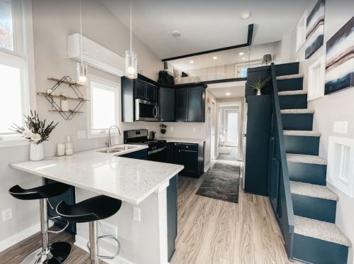 Modern kitchen with black cabinets, white countertops, and a staircase leading to an upper level. Bright and spacious design.