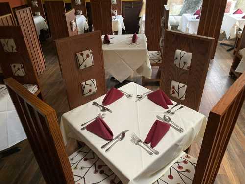 A cozy restaurant interior with neatly set tables, wooden partitions, and decorative tablecloths.