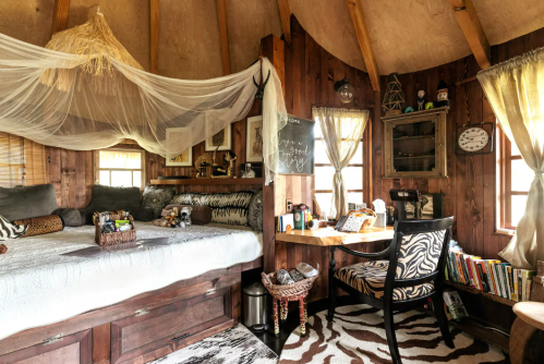 Cozy wooden room with a bed, desk, and decorative elements, featuring warm lighting and a rustic vibe.
