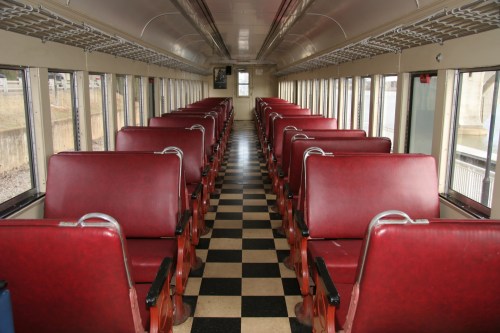 Interior of a vintage train car featuring red leather seats and a checkered floor, with large windows along the sides.