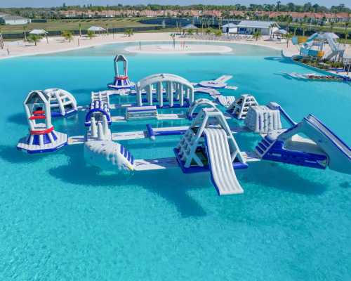 A large inflatable water park with slides and obstacles in a clear blue lagoon surrounded by palm trees.