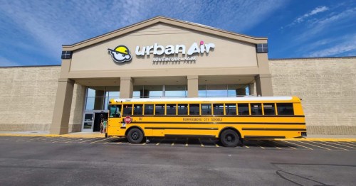 A yellow school bus parked in front of the Urban Air building on a sunny day.