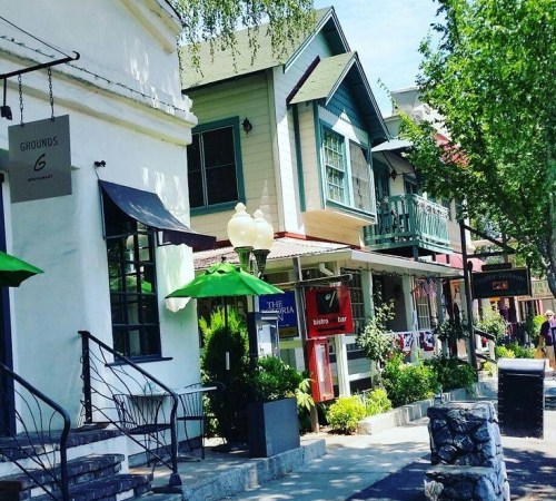 Charming street lined with colorful buildings, green umbrellas, and shops under a clear blue sky.