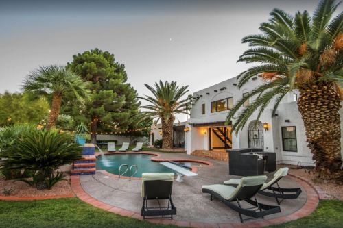 A serene backyard with a pool, lounge chairs, palm trees, and a modern house in the background.