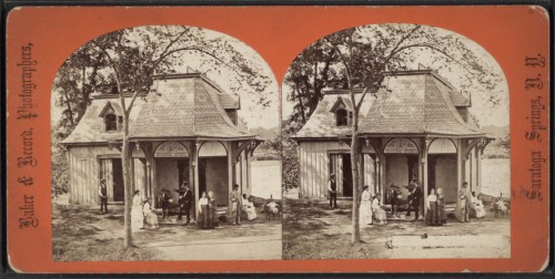 A vintage photograph of a wooden building with people gathered outside, set in a natural landscape.
