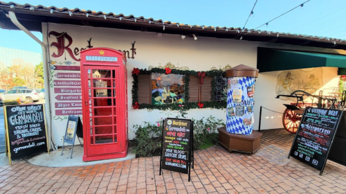 A colorful restaurant exterior featuring a red phone booth, festive decorations, and signage for a German deli.