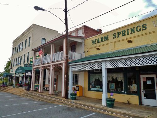 Historic buildings line a street in Warm Springs, featuring shops and a balcony with an American flag.