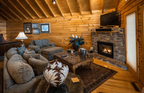 Cozy wooden living room with a stone fireplace, plush seating, and a coffee table, featuring warm lighting and decor.