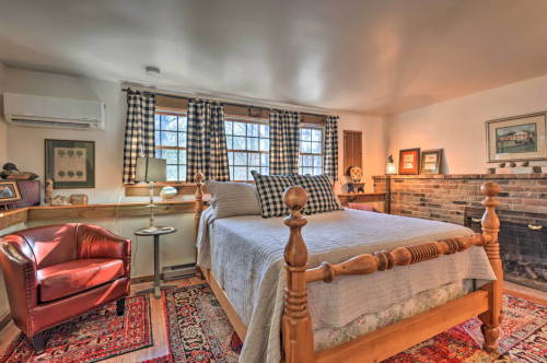Cozy bedroom featuring a wooden bed, checkered curtains, a red armchair, and a brick fireplace.