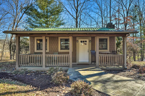 A cozy cabin with a green metal roof, front porch, and surrounded by trees on a sunny day.