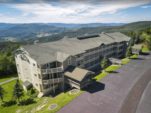 A large, multi-story building surrounded by green hills and mountains under a clear blue sky.