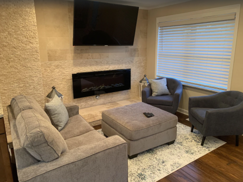Cozy living room with a gray sofa, two armchairs, a coffee table, and a modern fireplace beneath a TV.