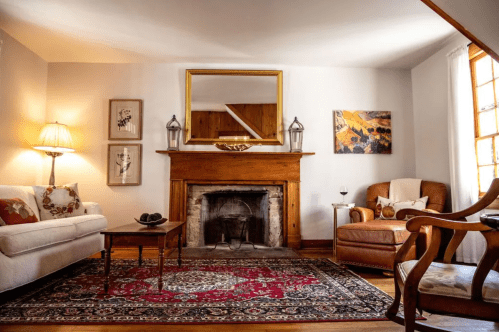 Cozy living room with a fireplace, wooden accents, a patterned rug, and comfortable seating. Warm, inviting atmosphere.