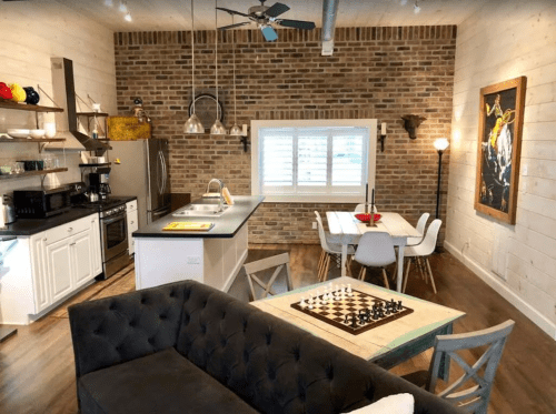 Modern kitchen and dining area with brick walls, wooden accents, and a chessboard on a coffee table.