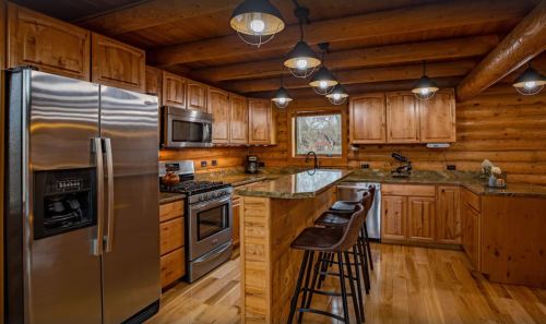 Cozy log cabin kitchen with wooden cabinets, stainless steel appliances, and a central island with bar stools.
