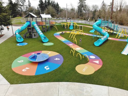 A colorful playground featuring slides, climbing structures, and a spinning game on a grassy area.