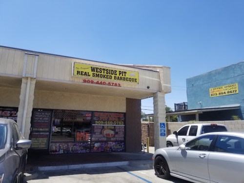 Exterior of Westside Pit BBQ restaurant with a bright sign, parked cars, and clear blue sky.