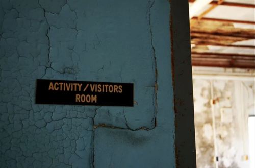 Sign on a cracked wall reads "Activity / Visitors Room," indicating a space within an abandoned building.