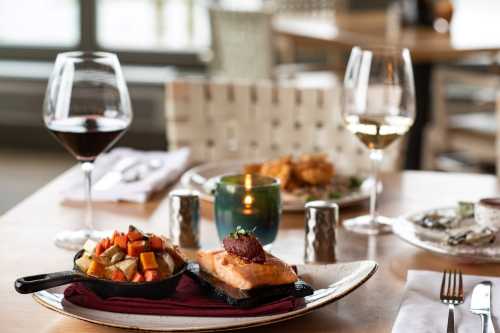 A beautifully plated dish with salmon and vegetables, accompanied by glasses of red and white wine on a dining table.