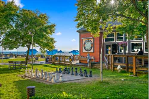 A large outdoor chess set in a grassy area near a colorful restaurant with blue umbrellas and a scenic view.