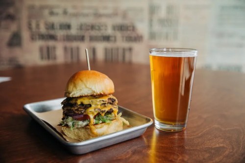 A juicy cheeseburger with lettuce, tomato, and a pint of beer on a wooden table.