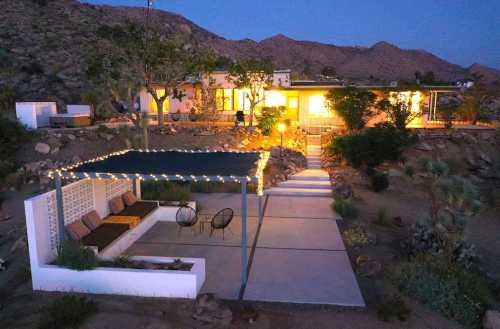 A modern desert home at dusk, featuring a cozy outdoor seating area with string lights and mountain views.