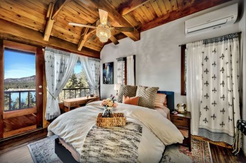 Cozy bedroom with wooden beams, large windows, and a view of nature, featuring a bed, nightstands, and decorative accents.