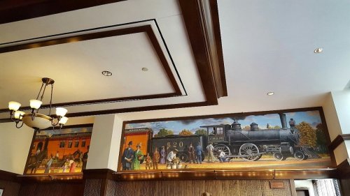 Mural depicting a historic steam locomotive and people in period attire, set in a warmly lit interior.