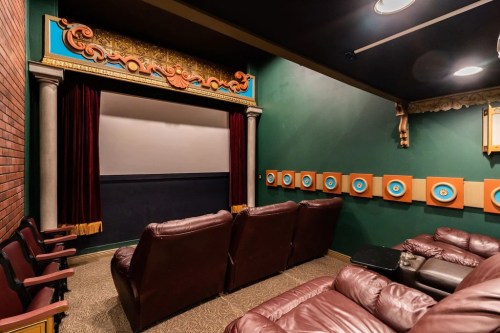 A cozy home theater with plush seating, a large screen, and decorative wall art in a dark green room.