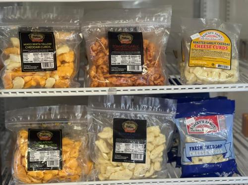 Various bags of cheese curds in different flavors, displayed on a shelf in a grocery store.
